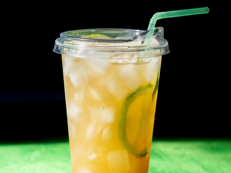 A clear cup filled with iced tea, lemon slices, and ice cubes, topped with a green straw.